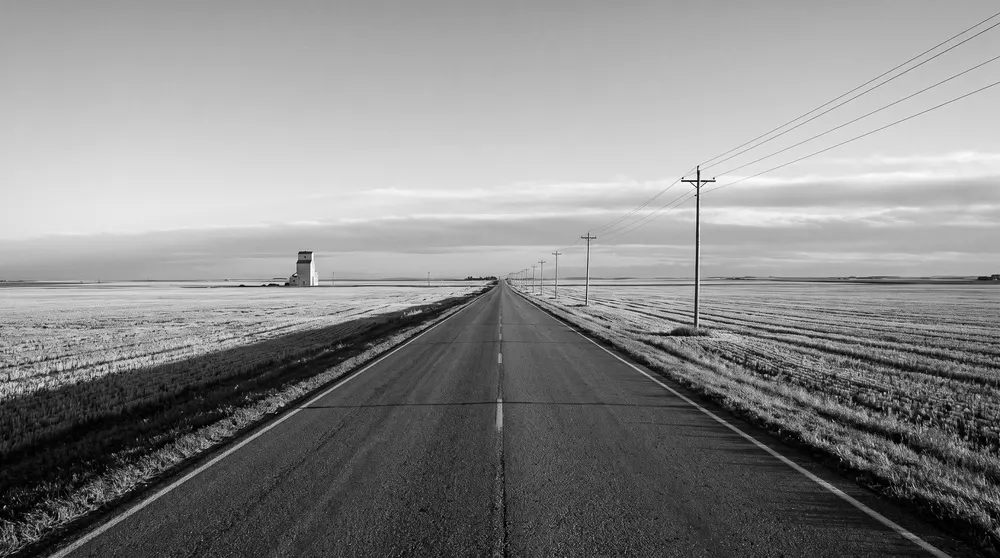 Straight two-lane prairie highway between harvested fields